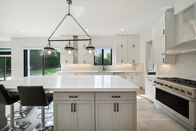 kitchen with wall chimney range hood, light hardwood / wood-style flooring, appliances with stainless steel finishes, a kitchen island, and a breakfast bar area