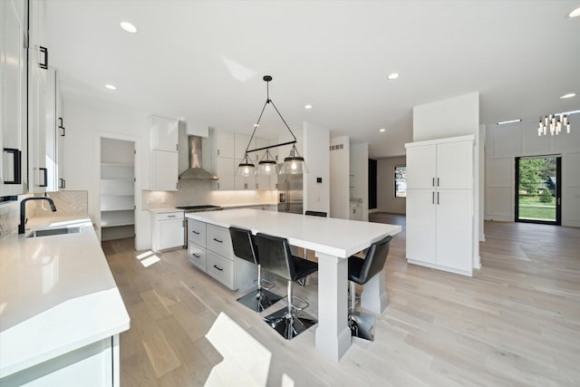 kitchen with pendant lighting, wall chimney exhaust hood, a kitchen island, and sink