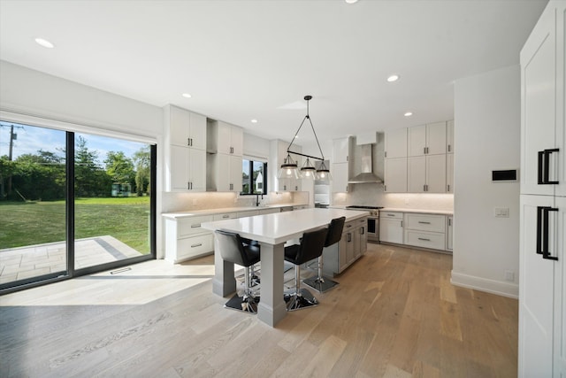 kitchen featuring pendant lighting, high end stainless steel range, wall chimney exhaust hood, light wood-type flooring, and white cabinetry