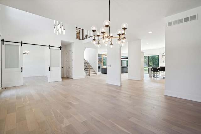 unfurnished dining area with a towering ceiling, a barn door, light hardwood / wood-style flooring, and a notable chandelier