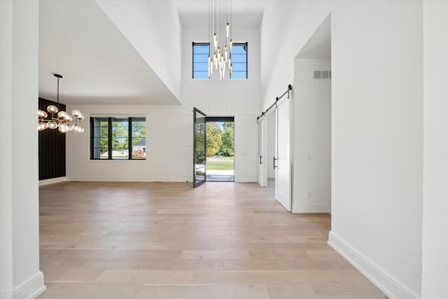 entryway featuring a barn door, light wood-type flooring, a high ceiling, and an inviting chandelier