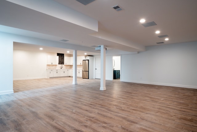 basement featuring stainless steel refrigerator and light hardwood / wood-style flooring