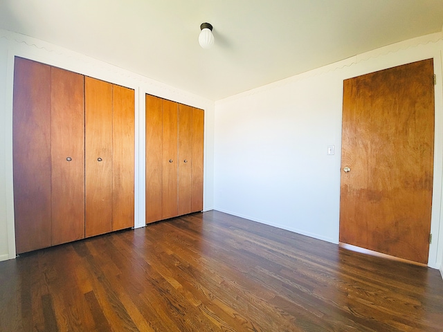 unfurnished bedroom featuring dark hardwood / wood-style floors and multiple closets