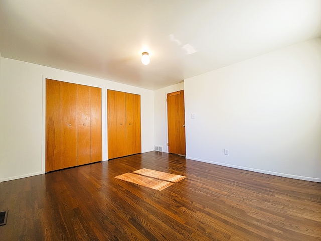 unfurnished bedroom with multiple closets and dark wood-type flooring