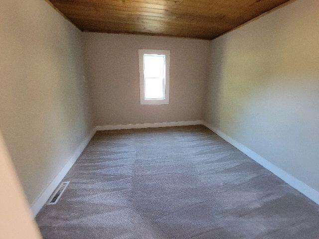 carpeted spare room with wood ceiling