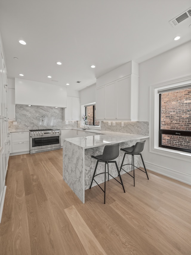 kitchen with range with two ovens, light stone countertops, light hardwood / wood-style floors, a kitchen bar, and white cabinetry