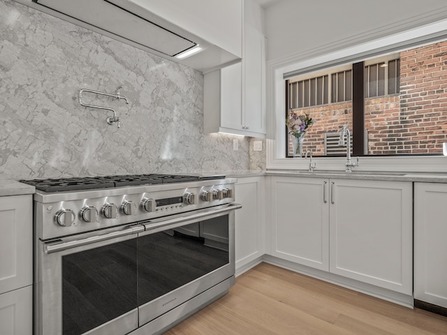 kitchen with white cabinets, decorative backsplash, light hardwood / wood-style floors, and high end stainless steel range