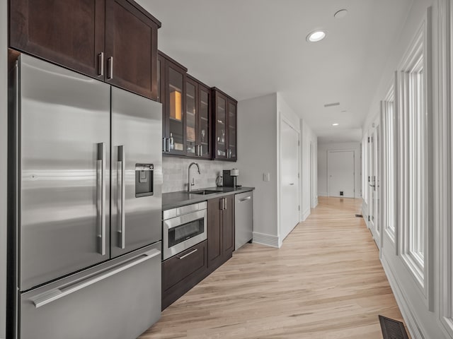 kitchen with backsplash, dark brown cabinetry, stainless steel appliances, sink, and light hardwood / wood-style floors