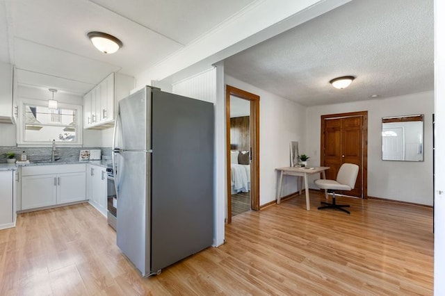 kitchen with sink, stainless steel appliances, a textured ceiling, white cabinets, and light wood-type flooring