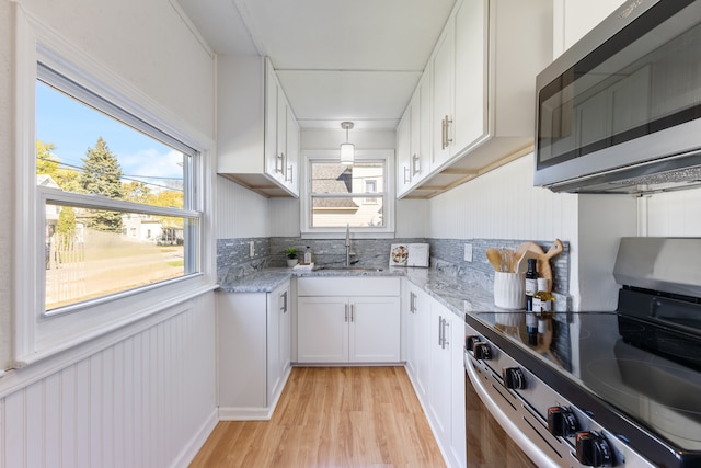 kitchen with appliances with stainless steel finishes, light hardwood / wood-style floors, white cabinetry, and a healthy amount of sunlight