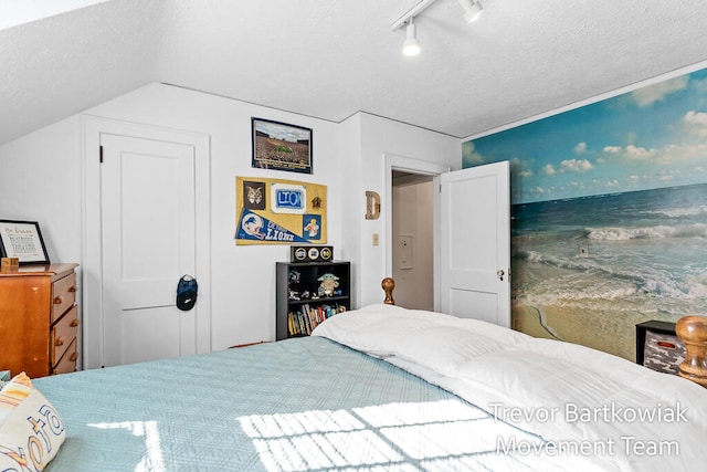 bedroom featuring lofted ceiling, a textured ceiling, and track lighting