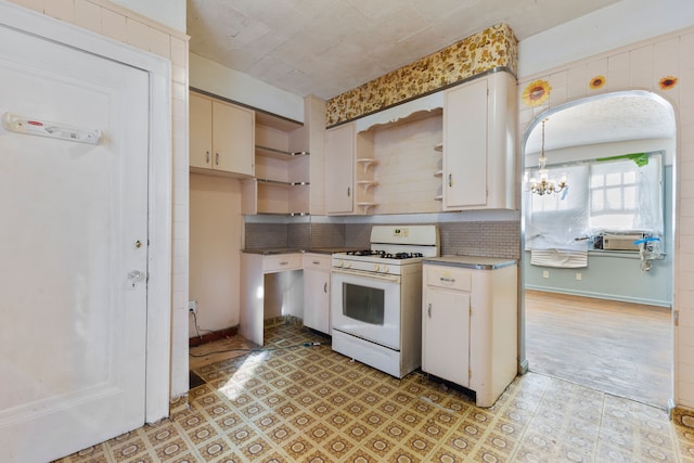 kitchen with tasteful backsplash, white gas range, pendant lighting, a notable chandelier, and white cabinetry