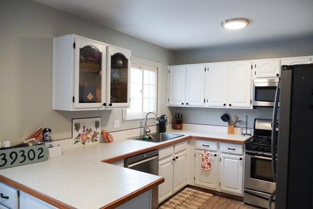 kitchen with kitchen peninsula, light wood-type flooring, stainless steel appliances, sink, and white cabinets