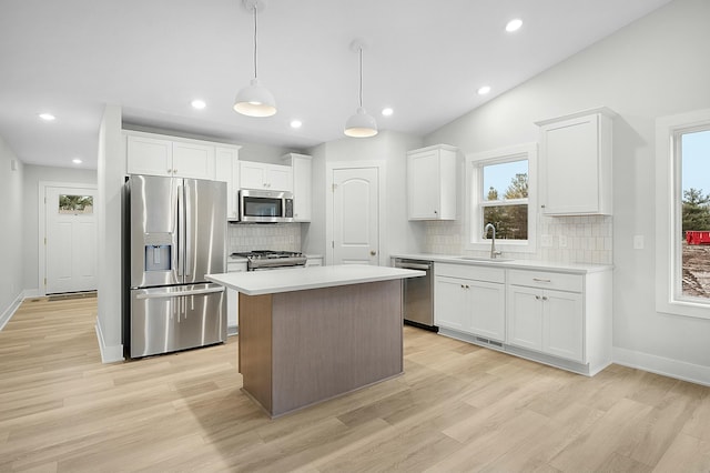 kitchen featuring white cabinetry, stainless steel appliances, vaulted ceiling, decorative light fixtures, and a kitchen island