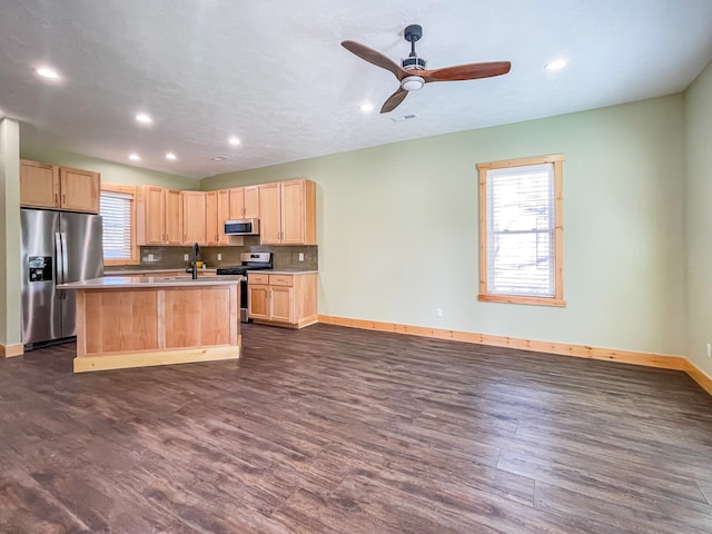 kitchen featuring light brown cabinets, a kitchen island with sink, dark wood-type flooring, ceiling fan, and appliances with stainless steel finishes