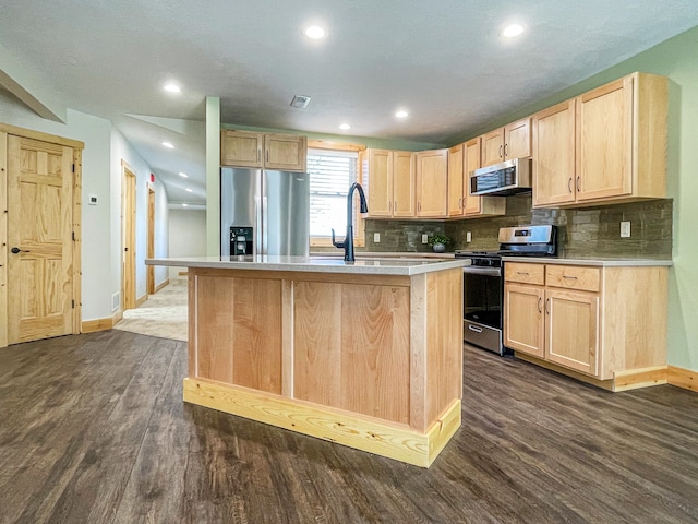 kitchen with light brown cabinetry, dark wood-type flooring, appliances with stainless steel finishes, and an island with sink