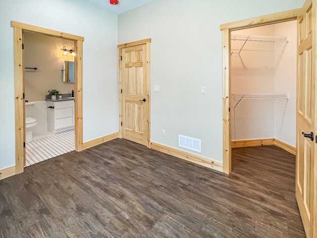 unfurnished bedroom with dark hardwood / wood-style floors, a walk in closet, ensuite bathroom, and a closet