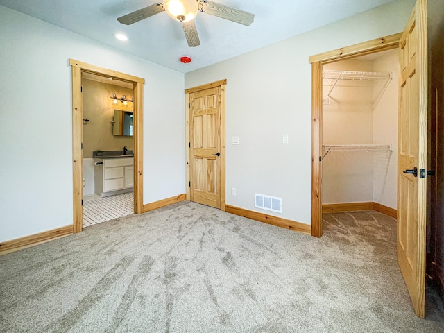 unfurnished bedroom featuring a closet, a walk in closet, light colored carpet, and ceiling fan