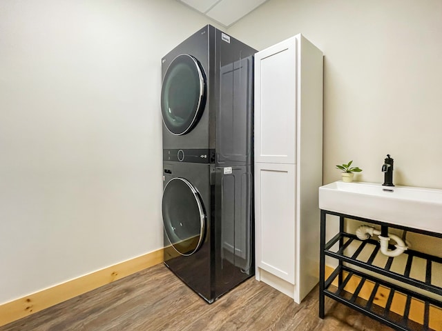 washroom with cabinets, hardwood / wood-style flooring, and stacked washer and clothes dryer