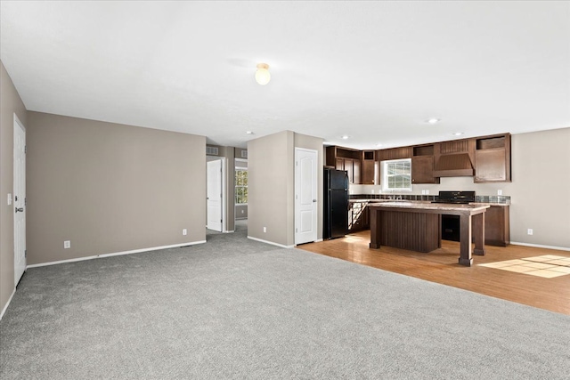 kitchen with black fridge, a center island, dark brown cabinets, and light wood-type flooring