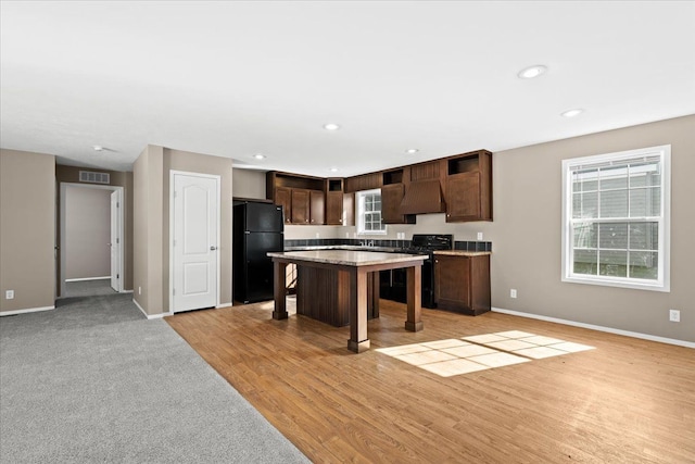 kitchen featuring light wood-type flooring, a breakfast bar, dark brown cabinetry, black appliances, and a kitchen island