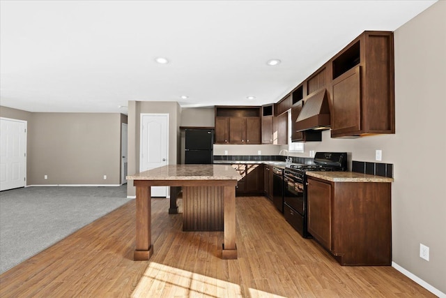 kitchen featuring black appliances, a center island, custom range hood, and light hardwood / wood-style floors