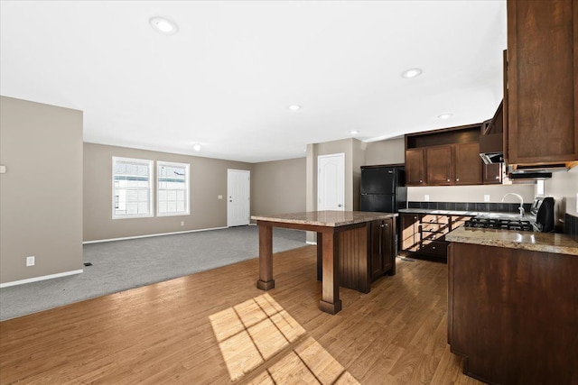 kitchen featuring black fridge, light stone counters, light hardwood / wood-style floors, a breakfast bar area, and a kitchen island