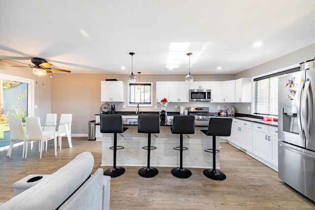 kitchen featuring stainless steel appliances, pendant lighting, a kitchen bar, white cabinets, and light wood-type flooring