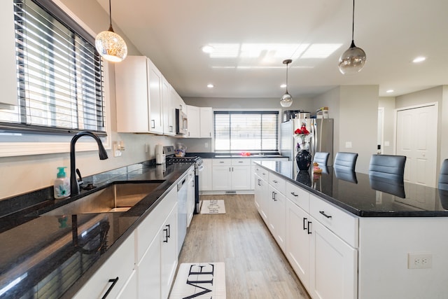 kitchen with pendant lighting, dark stone counters, light hardwood / wood-style flooring, appliances with stainless steel finishes, and white cabinetry