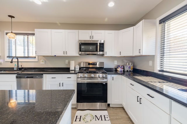 kitchen featuring sink, dark stone counters, decorative light fixtures, white cabinets, and appliances with stainless steel finishes