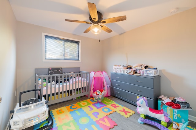 bedroom featuring a nursery area, light hardwood / wood-style floors, and ceiling fan