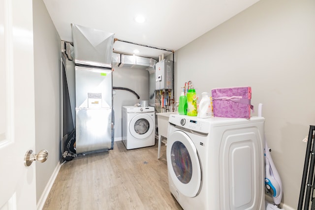 clothes washing area with light wood-type flooring, tankless water heater, heating unit, and washer and clothes dryer