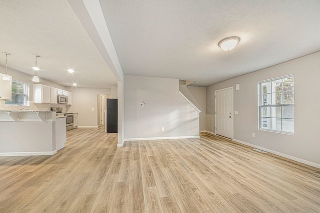 unfurnished living room with a textured ceiling and light hardwood / wood-style floors