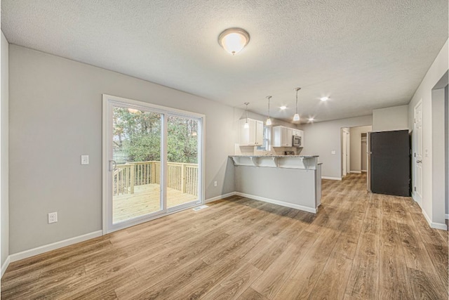 kitchen with hanging light fixtures, kitchen peninsula, light wood-type flooring, white cabinets, and appliances with stainless steel finishes