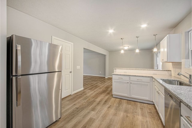 kitchen with hanging light fixtures, sink, appliances with stainless steel finishes, white cabinetry, and kitchen peninsula