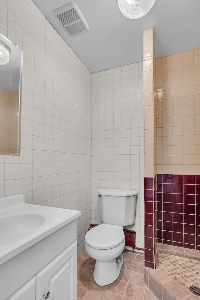 bathroom with tile patterned floors, vanity, a shower, tile walls, and toilet