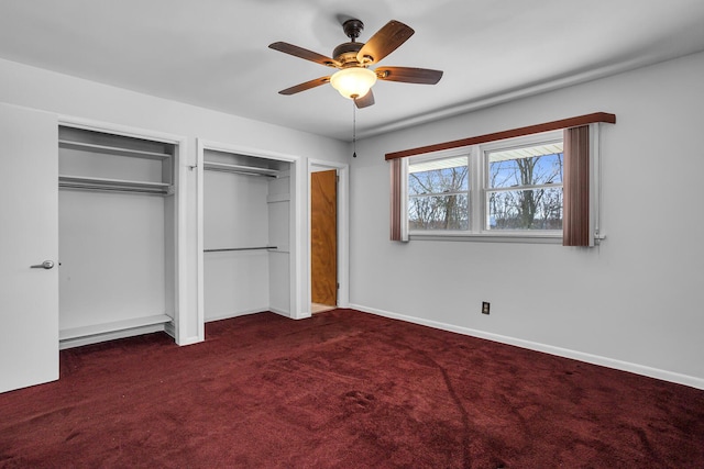 unfurnished bedroom with ceiling fan, two closets, and dark colored carpet