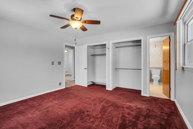 unfurnished bedroom featuring ceiling fan, dark carpet, multiple closets, and ensuite bath