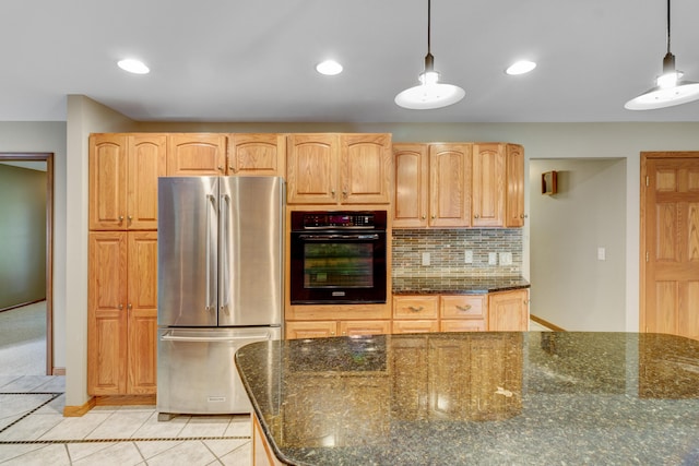 kitchen with decorative light fixtures, oven, stainless steel refrigerator, and dark stone counters