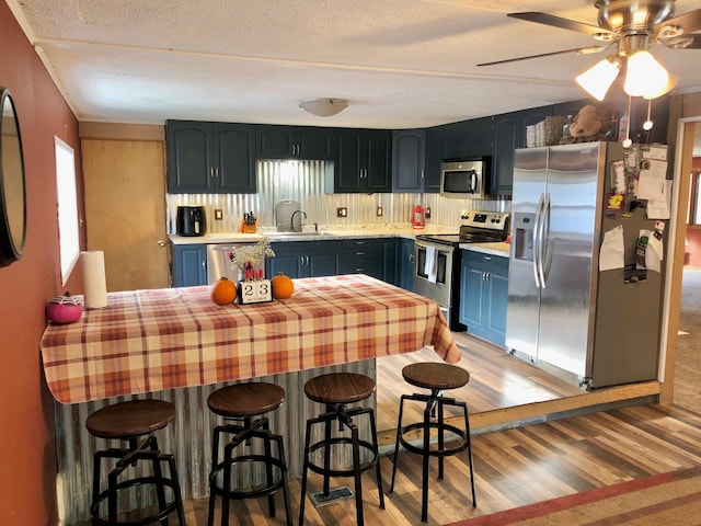 kitchen with ceiling fan, light hardwood / wood-style floors, blue cabinets, and appliances with stainless steel finishes