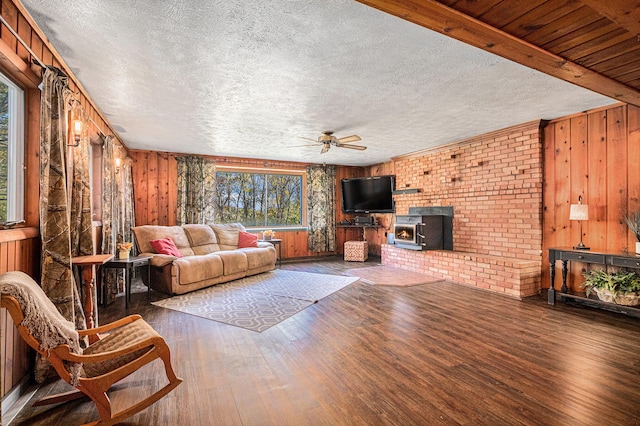 living room with ceiling fan, wood walls, a wood stove, and dark wood-type flooring