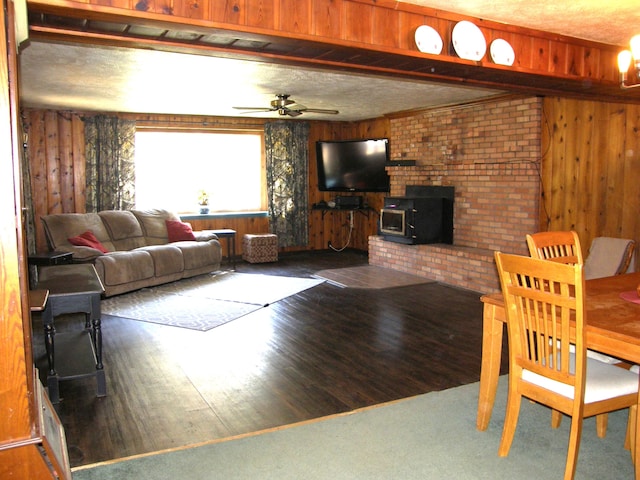 living room featuring ceiling fan, wood walls, a wood stove, and a textured ceiling