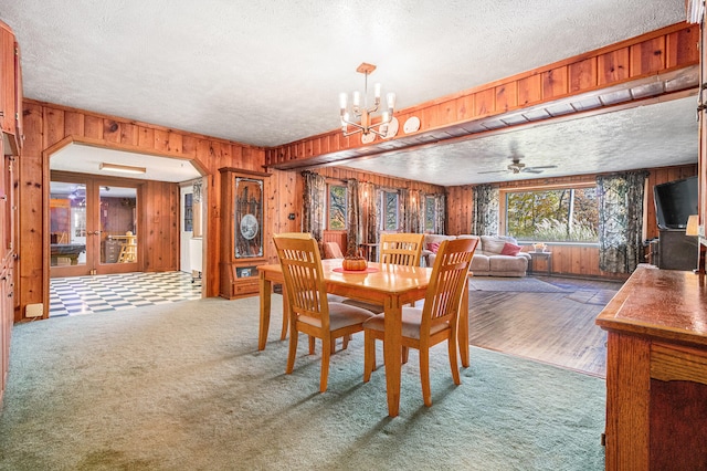 carpeted dining area with a textured ceiling, wood walls, and ceiling fan with notable chandelier