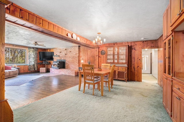 carpeted dining room with a textured ceiling, a wood stove, and ceiling fan with notable chandelier