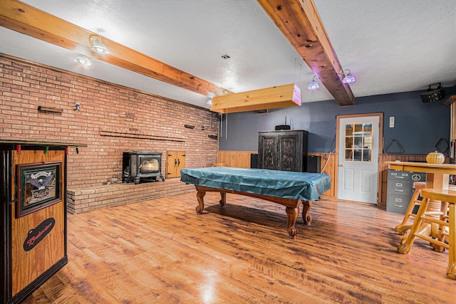 game room featuring wood walls, a wood stove, a textured ceiling, beam ceiling, and brick wall