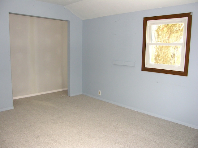 unfurnished bedroom featuring light carpet, a closet, and lofted ceiling