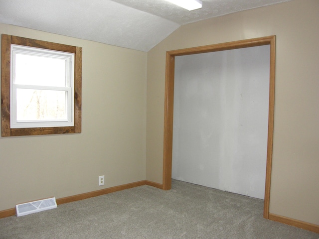 unfurnished bedroom featuring lofted ceiling, a textured ceiling, and light carpet