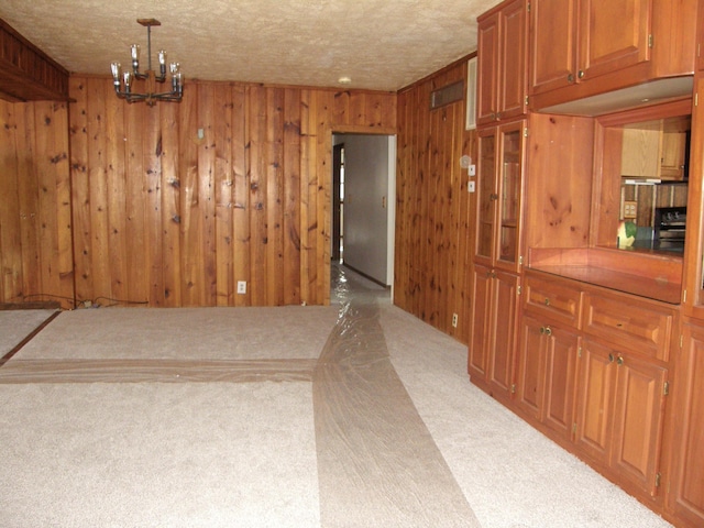 dining space featuring light carpet, wood walls, a textured ceiling, and an inviting chandelier