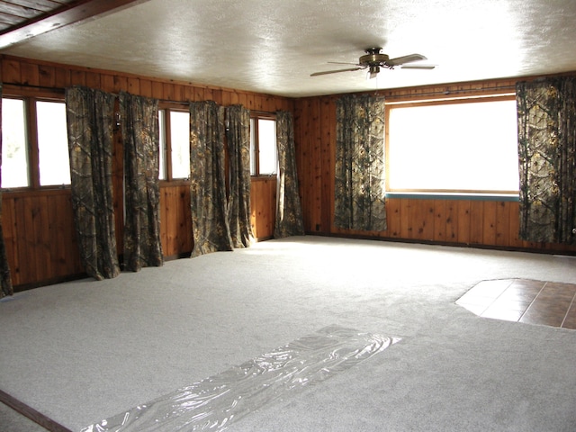 unfurnished room featuring carpet flooring, a textured ceiling, ceiling fan, and wood walls