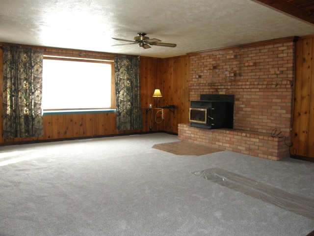 unfurnished living room featuring a wood stove, wood walls, ceiling fan, and a textured ceiling